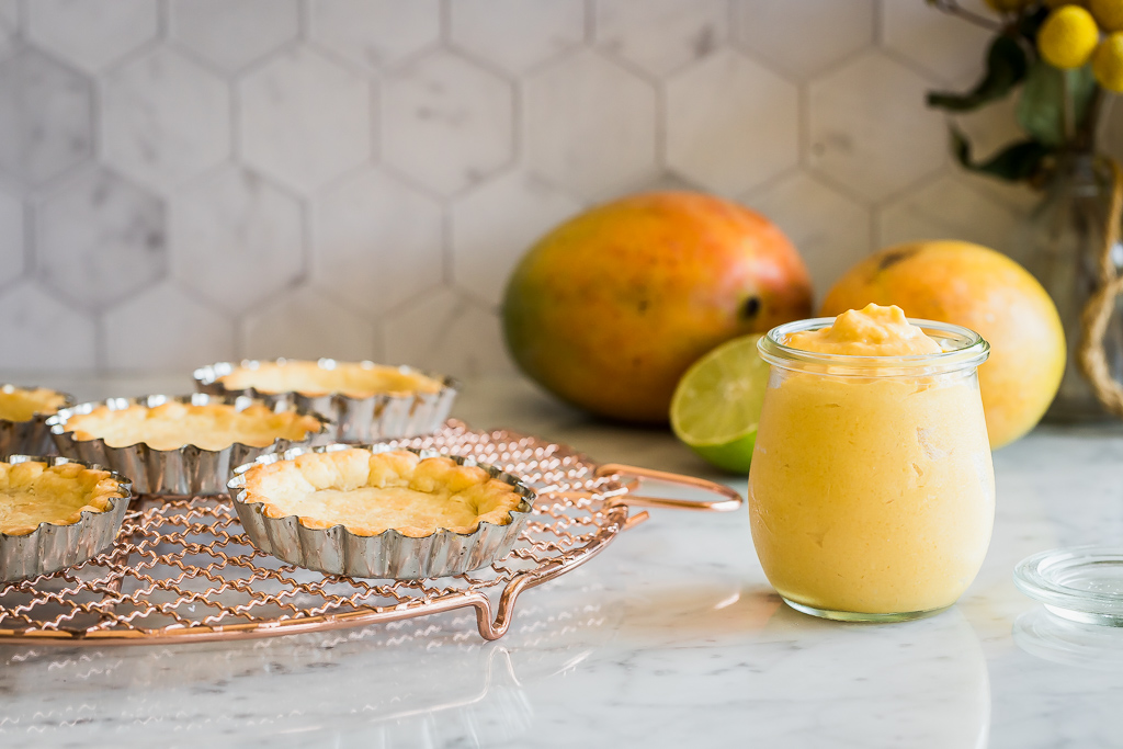 a jar of mango curd next to some freshly baked tart shells