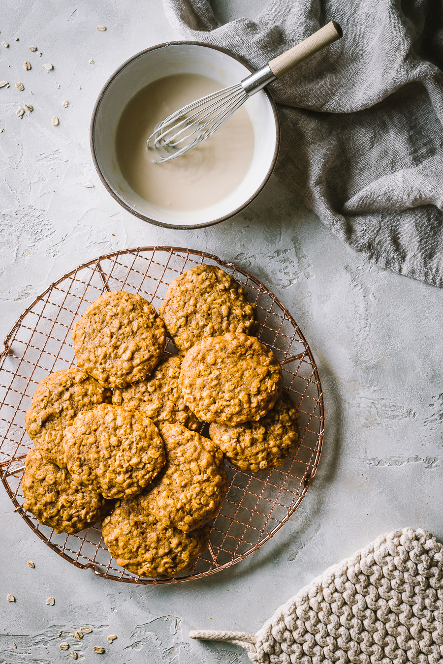 a pile of unglazed pumpkin oatmeal cookies next to a small dish with maple icing
