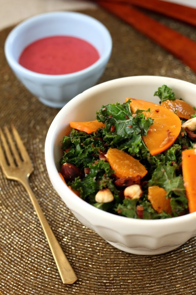 a small bowl of winter kale salad with persimmon slices next to a small dish with cranberry dressing 