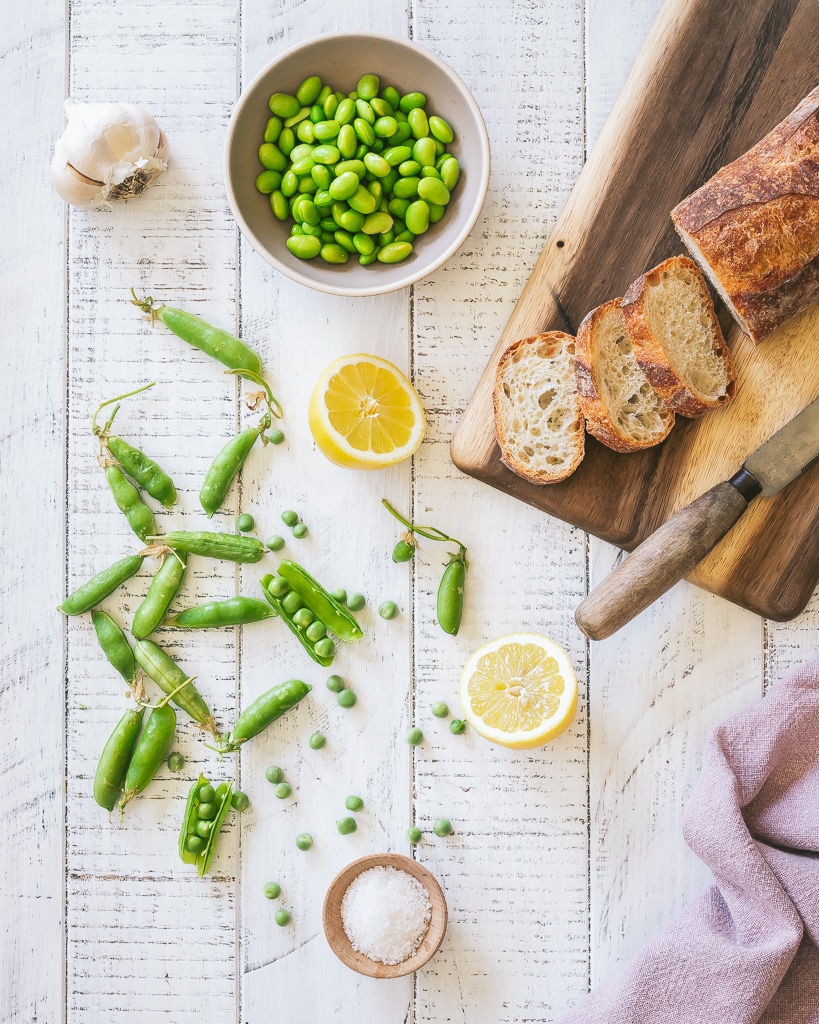 shelled peas and edamame with sliced bread on a cutting board