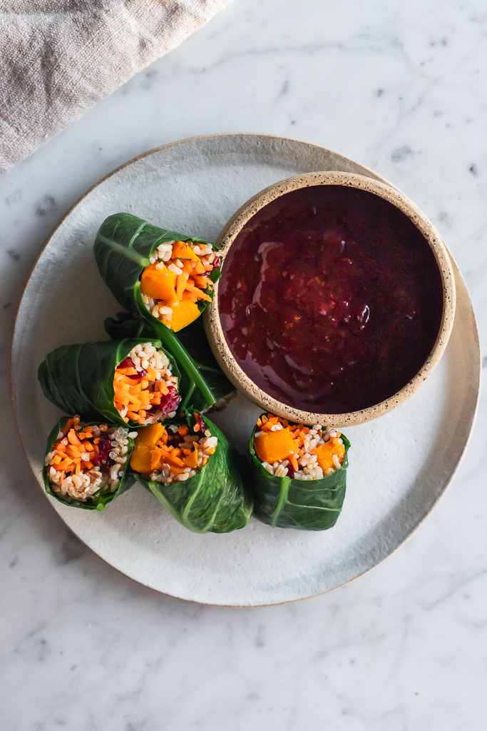 a white ceramic plate with collard green rolls and a bowl of cranberry dipping sauce