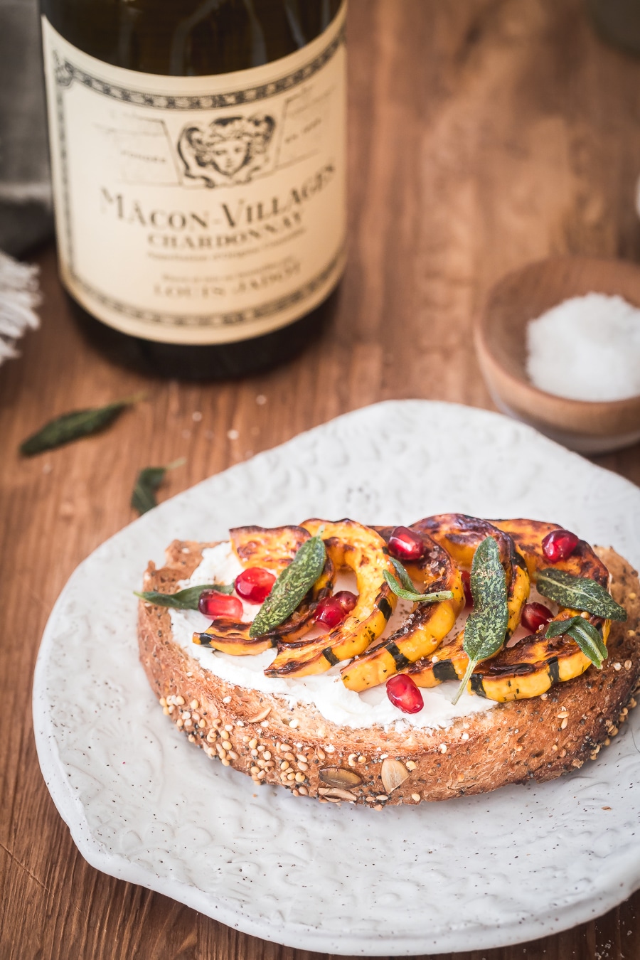 a slice of toasted multigrain bread topped with goat cheese, roasted squash and pomegranate arils