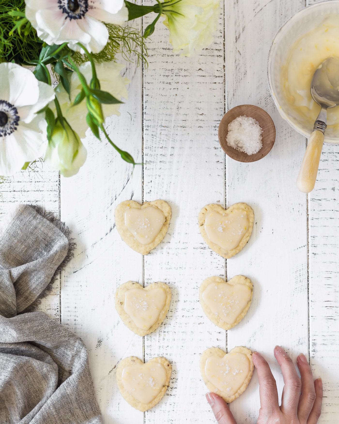 a hand grabbing a Lavender Sea Salt Shortbread Cookies with Grapefruit Icing off a white rustic table