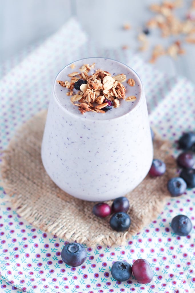 a Blueberry Crisp Collagen Smoothie decorated with granola next to fresh blueberries 