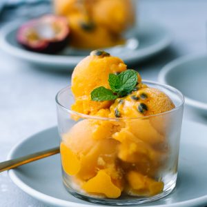 Scoops of Mango Passion Fruit Sorbet with fresh mint and passion fruit in a clear glass