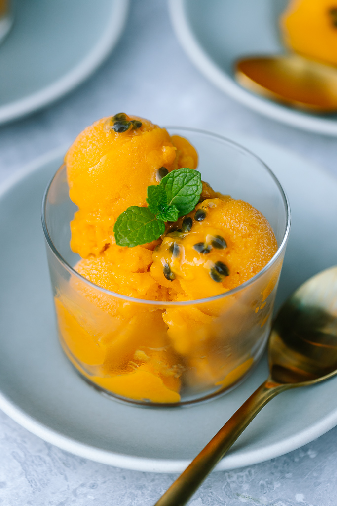 Scoops of Mango Passion Fruit Sorbet with fresh mint and passion fruit in a clear glass