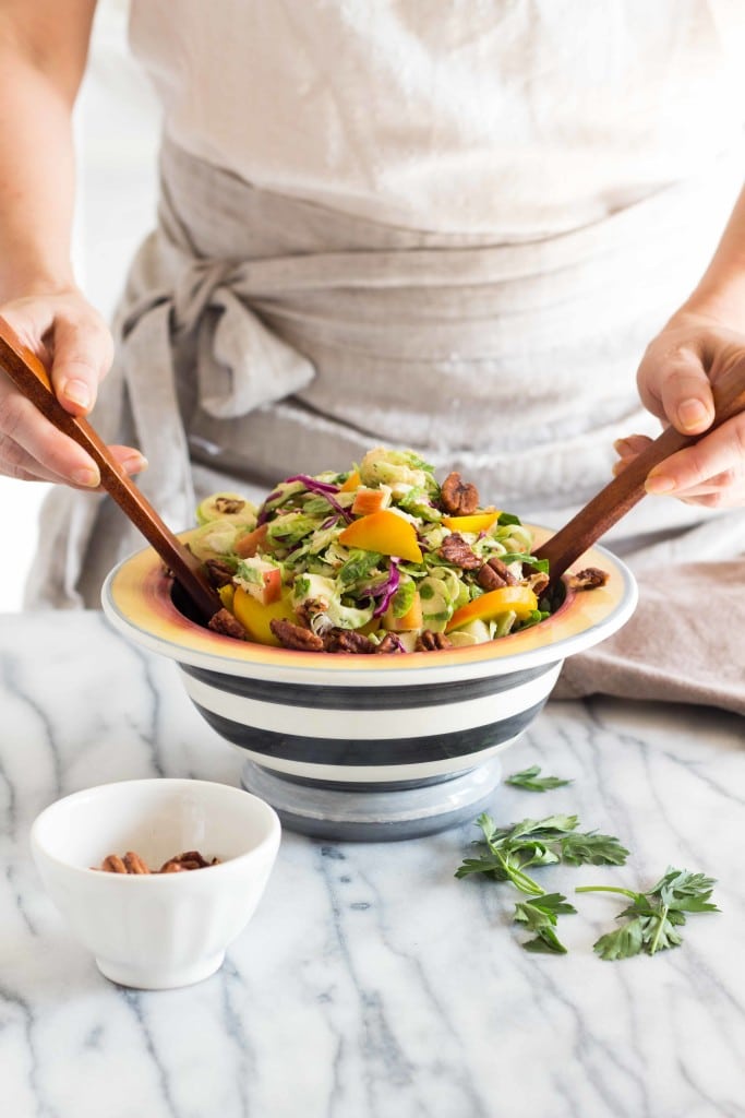 Autumn Brussels Sprout Slaw with golden beets and red cabbage being tossed in a striped salad bowl
