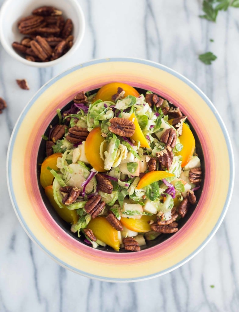 overhead shot of Autumn Brussels Sprout Slaw on a marble countertop with a small side dish of pecans