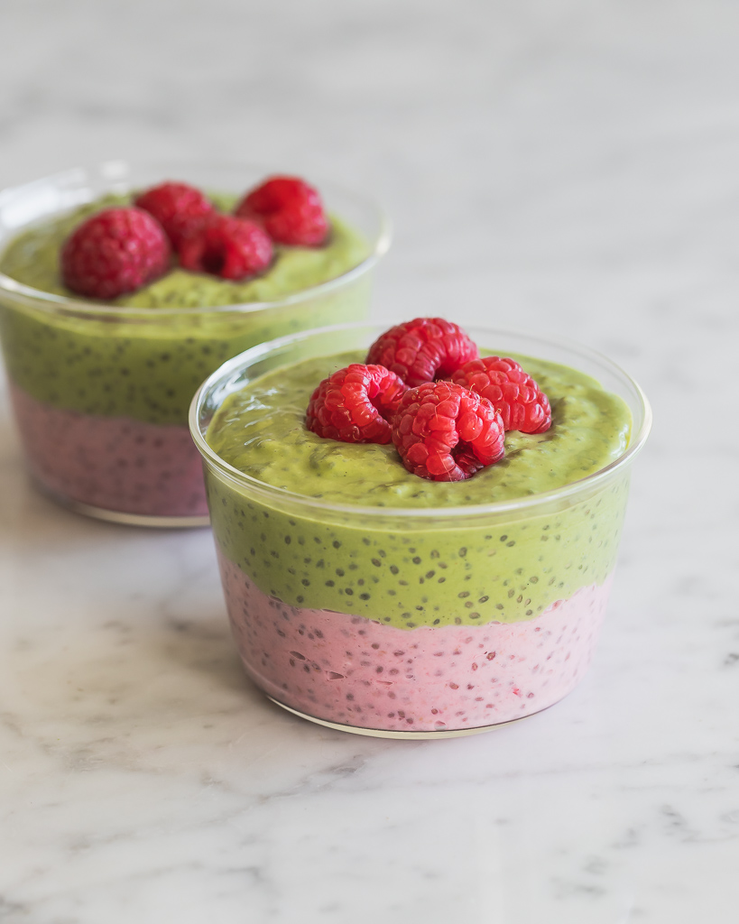 two dessert jars with layered raspberry chia pudding and matcha chia pudding topped with fresh raspberries