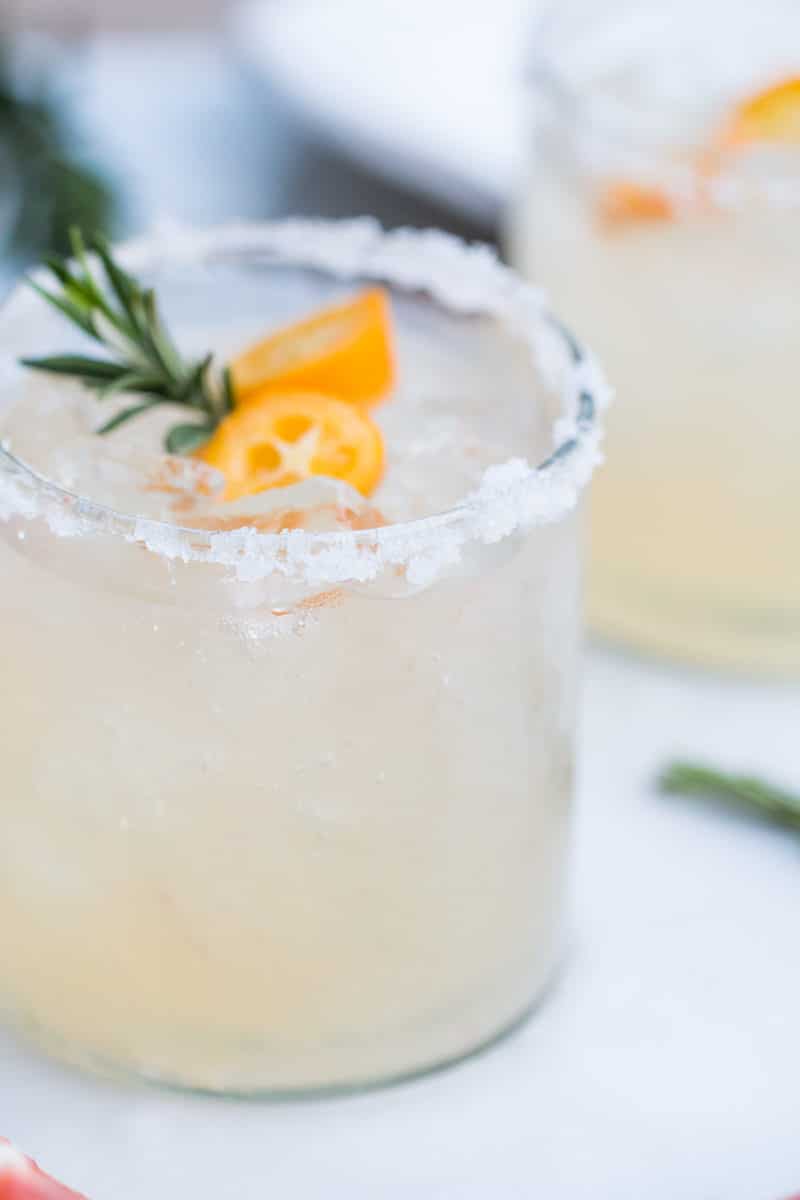 close-up side view of a salt-rimmed cocktail glass with Rosemary Kumquat Paloma
