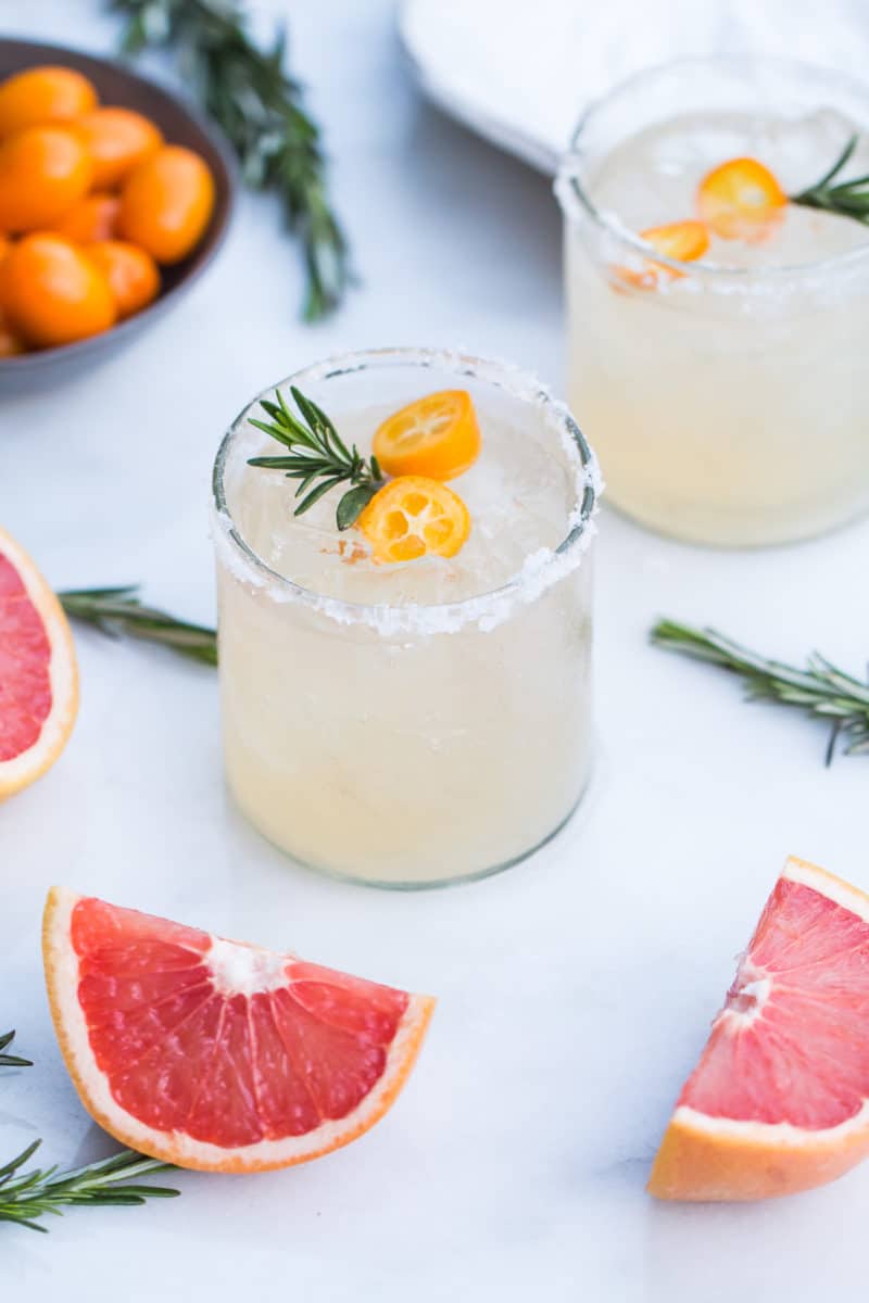 side view of a Rosemary Kumquat Paloma cocktail decorated with rosemary twigs and sliced kumquats
