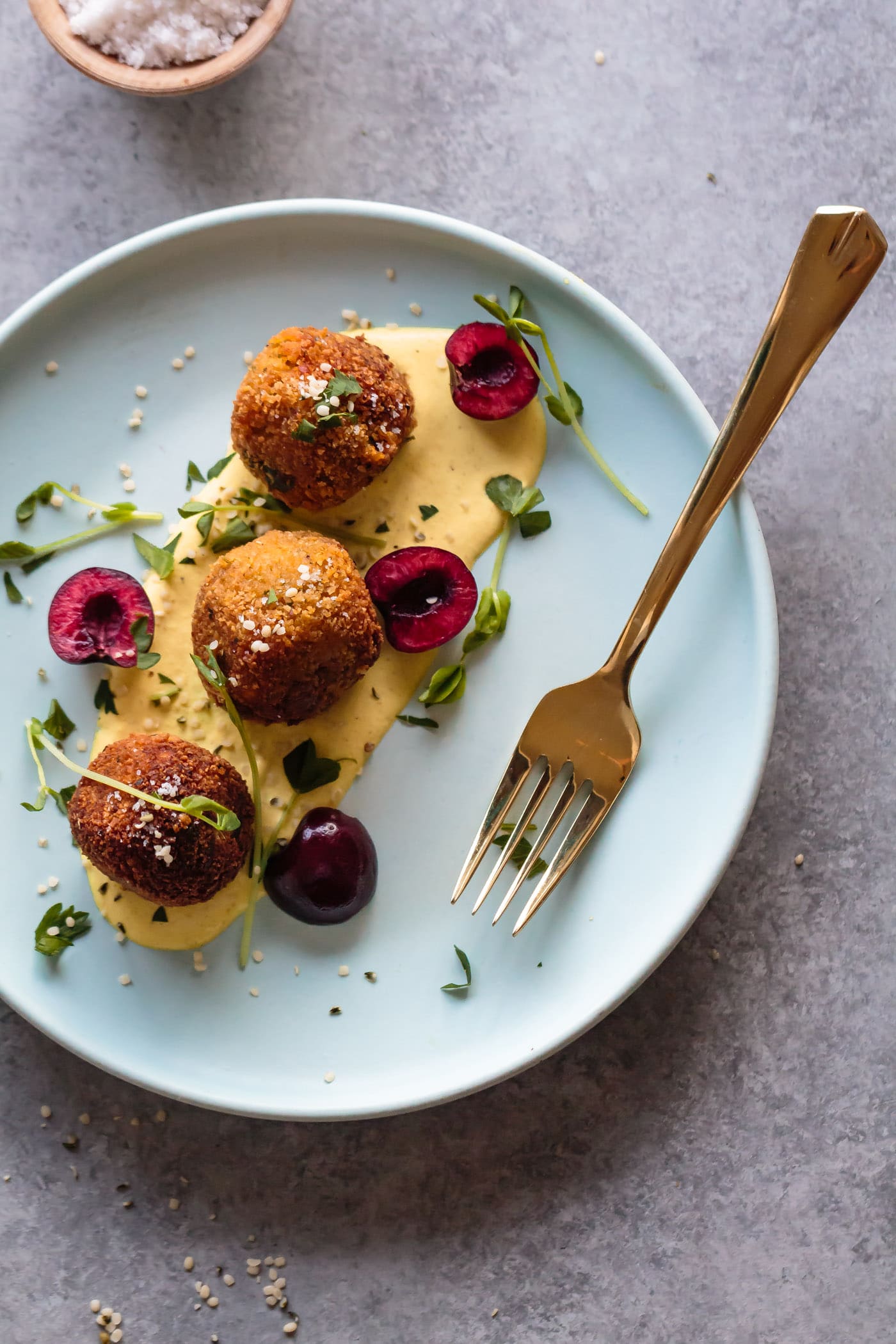 Vegan Sweet Potato Fritters with Split Red Lentils served on Curried Cashew Cream and decorated with fresh cherries and microgreend