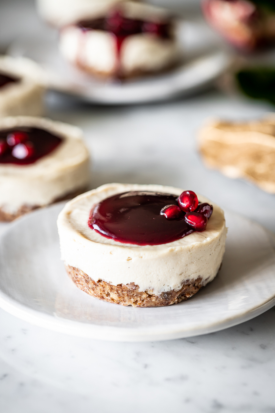 side view of mini vegan cheesecake with pomegranate glaze on a white plate