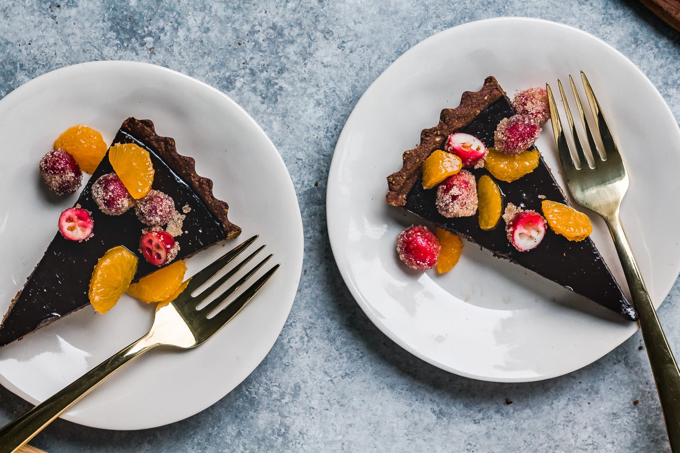 close up of slices of dark chocolate tart with sugared cranberry and satsumas
