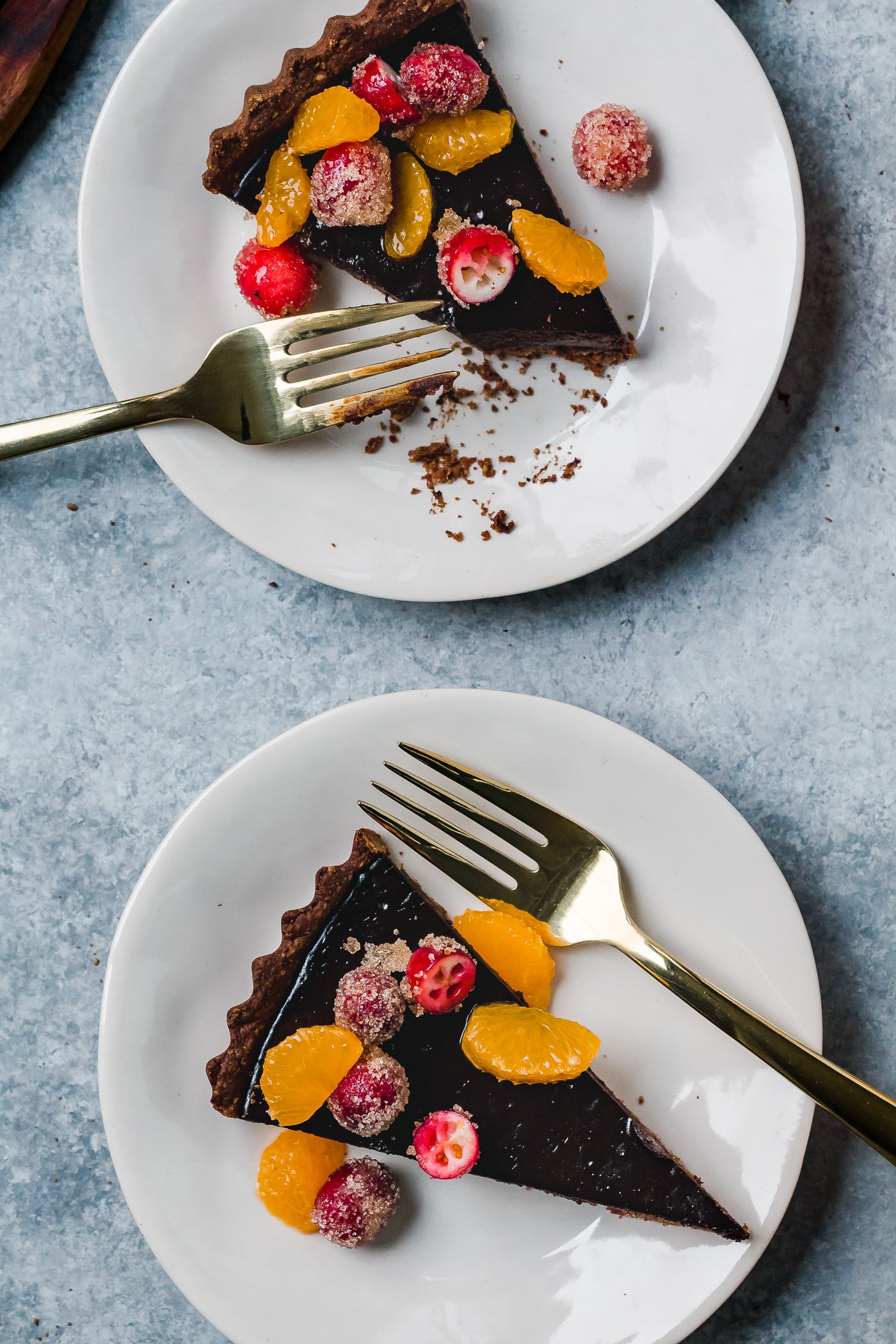 close up of slices of dark chocolate tart with cinnamon sugared cranberry and satsumas