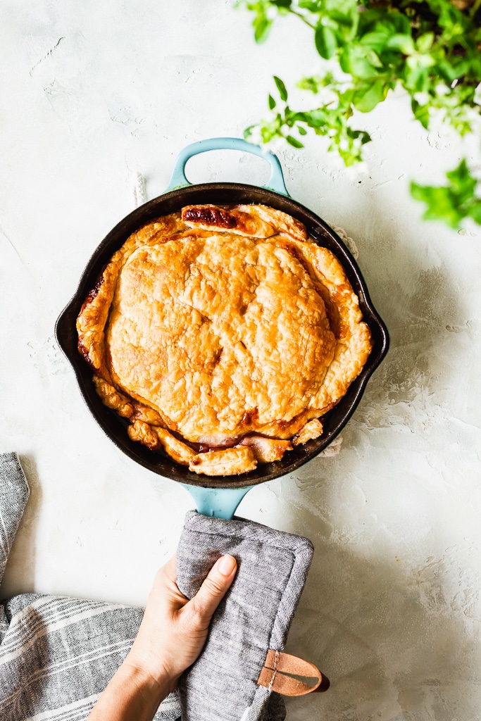 a woman holding a freshly baked plum tarte tatin in a skillet over a marble kitchen counter