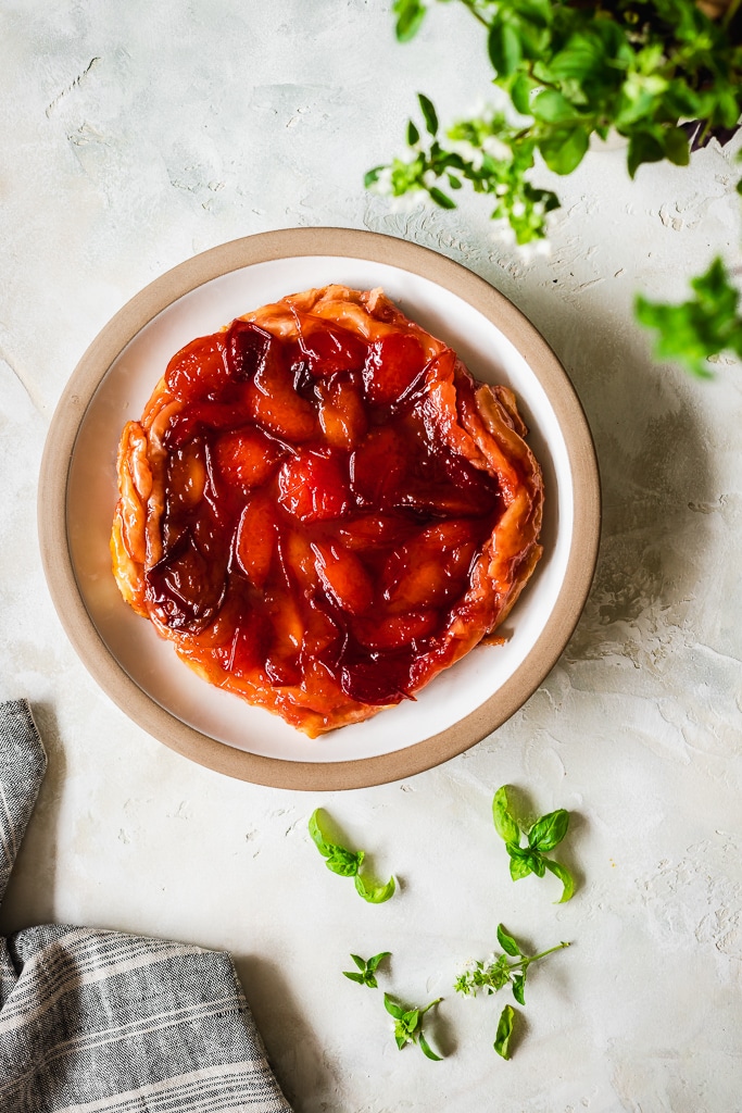 overhead shot of a homemade plum and basil tarte tatin with fresh basil in the background