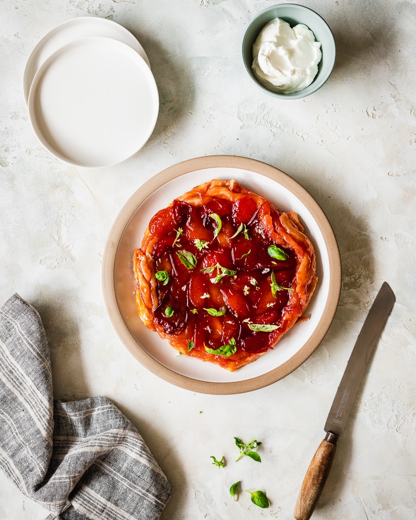 overhead shot of an Easy Tarte Tatin with plums and basil on a white marble kitchen table 