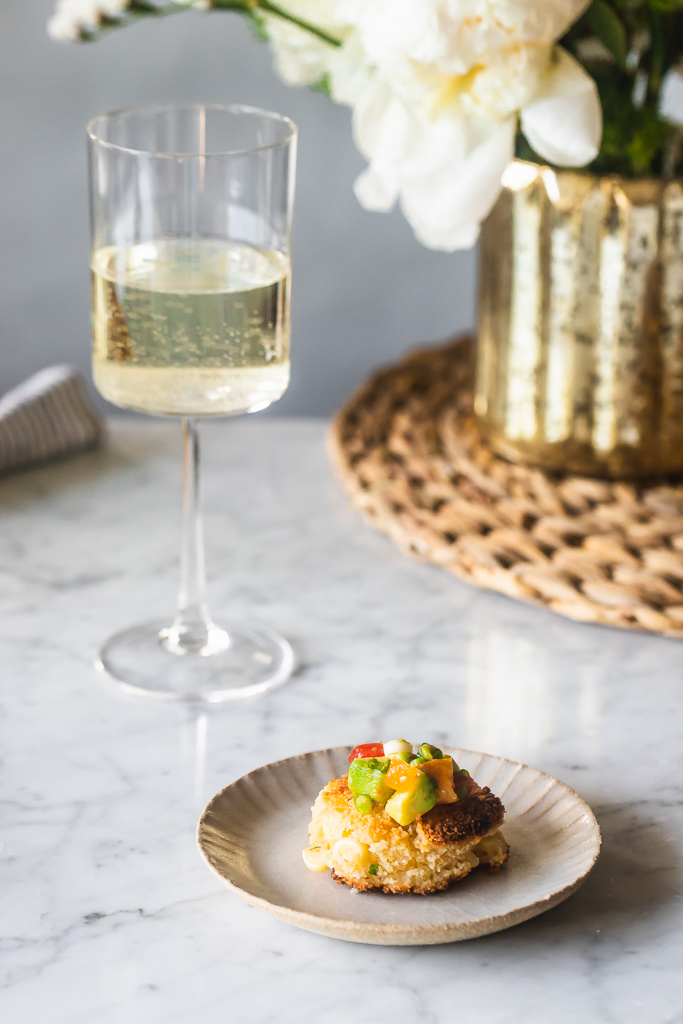 corn and goat cheese fritter on an appetizer plate with a glass of white wine