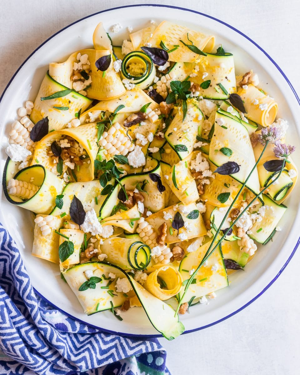 Marinated zucchini salad with corn, herbs, feta and walnuts on a round white plate