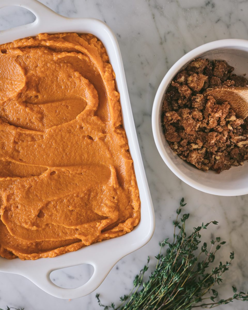 Sweet Potato Casserole spread into a white baking dish with a bowl of pecan streusel and a bunch of thyme sprigs