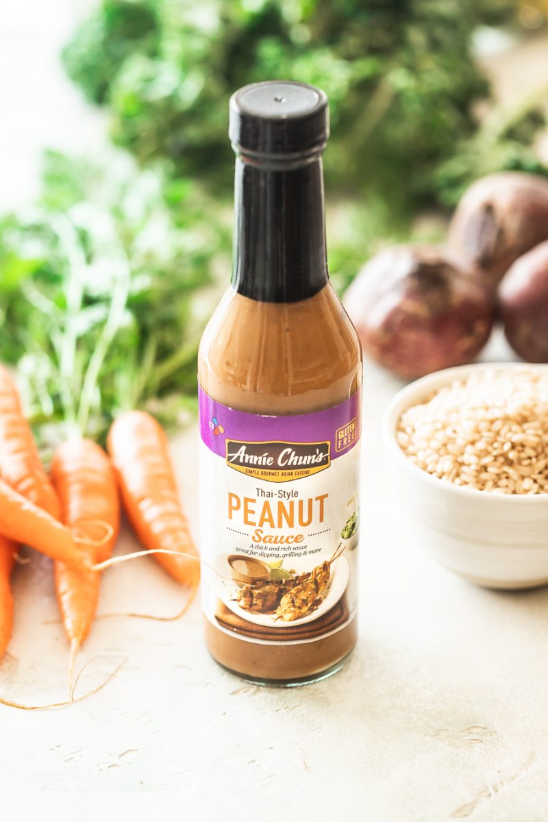 a bottle of peanut sauce with fresh vegetables and uncooked brown rice