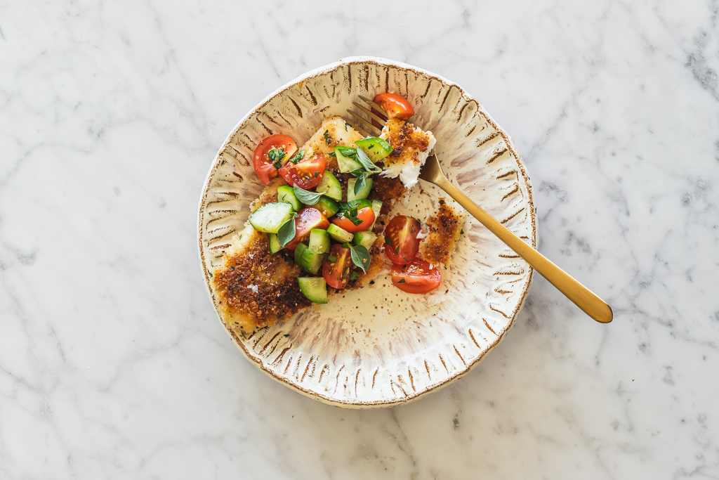a plate with a panko crusted halibut filet served topped with a side of cucumber tomato salad