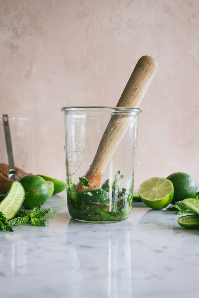 cucumber mojito ingredients being muddled in a glass jar