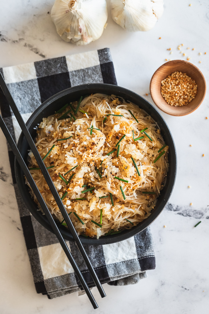 a bowl of sesame garlic noodles with crispy rice, chives and toasted sesame seeds