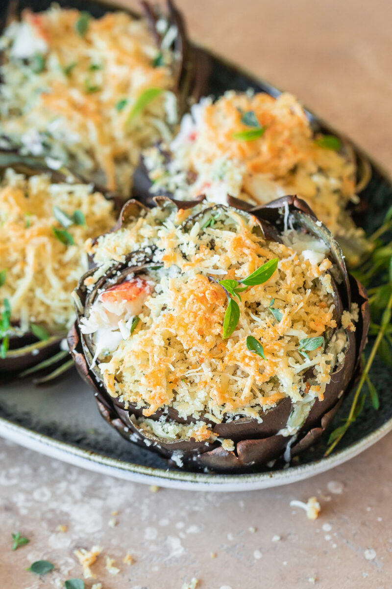 close up of a purple artichoke stuffed with crab and spinach dip and topped with breadcrumbs and Parmesan.