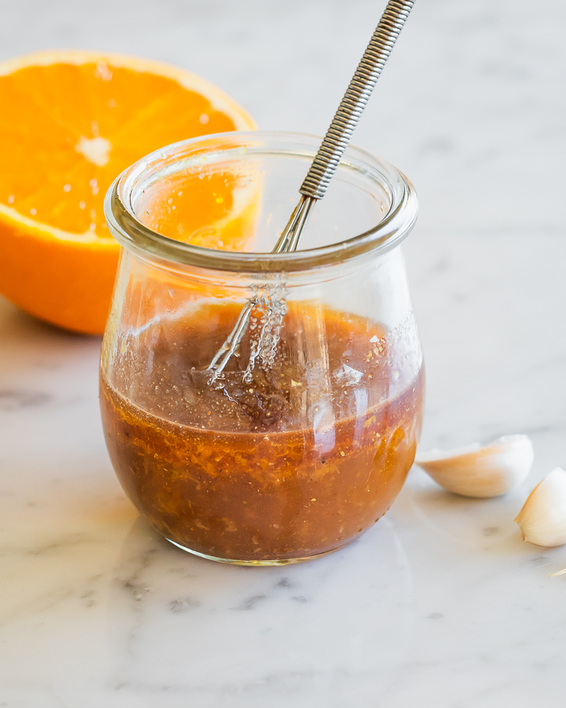 Moroccan Orange Salad Dressing in a small mason jar with 2 garlic cloves and a halved orange in the background
