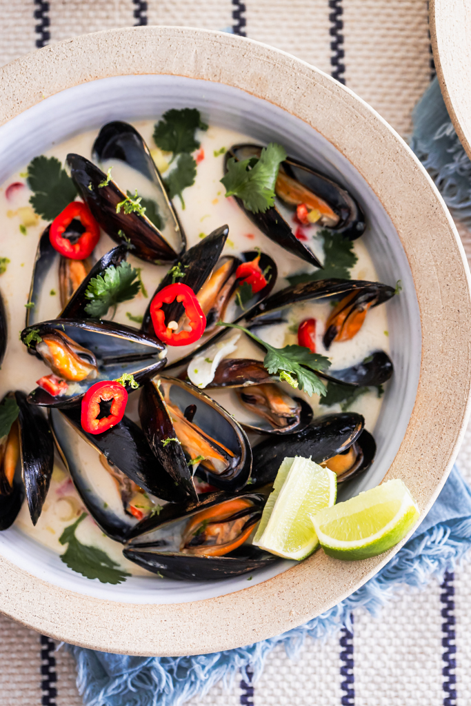 a close up view of lemongrass coconut steamed mussels with fresh lime wedges served on the side