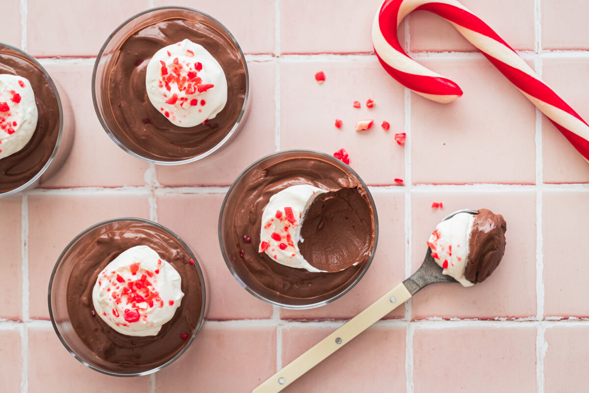 overhead view of chocolate peppermint mousse cups with candy cane and spoonful of mousse off to the side on pink tiles