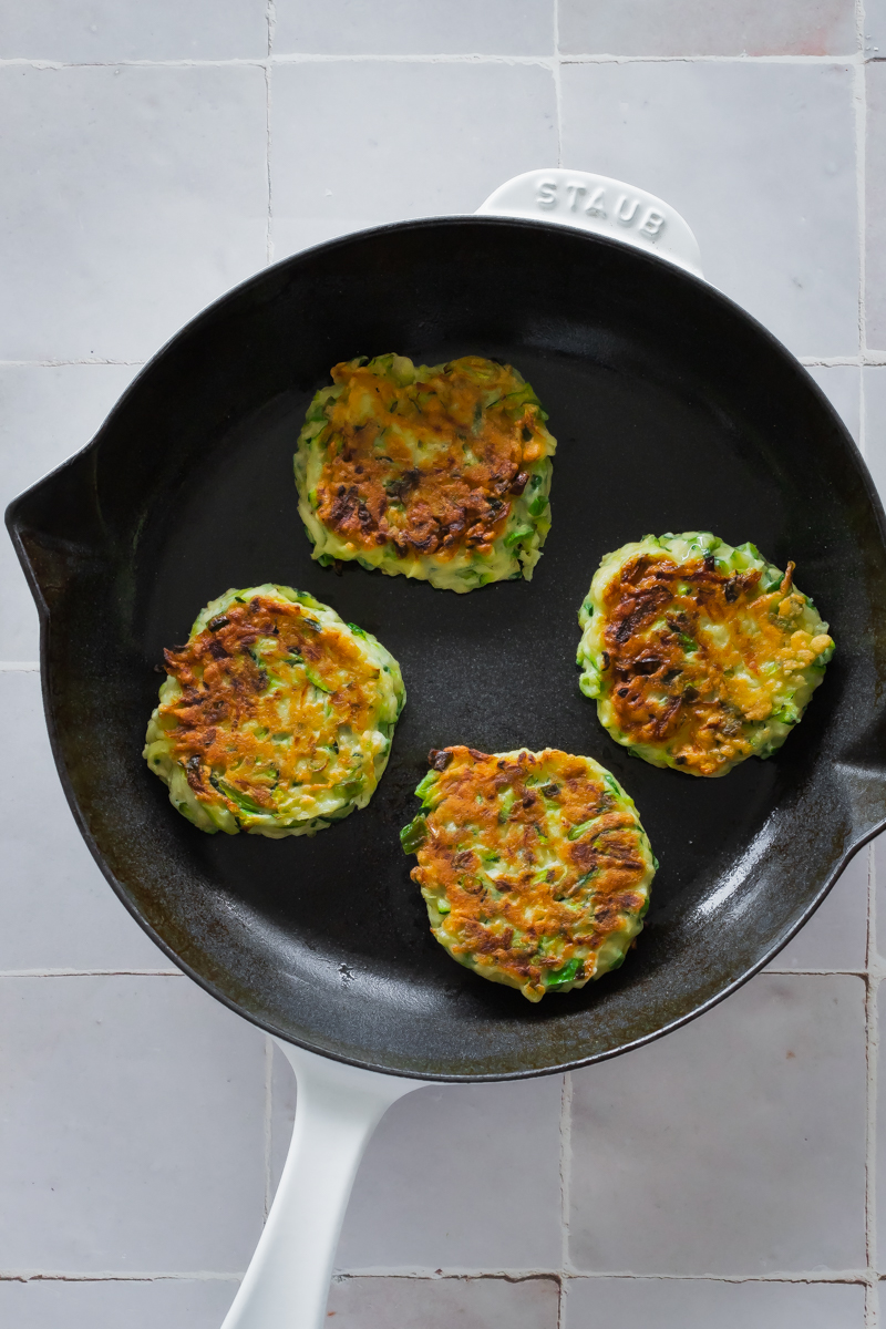 four zucchini fritters in a white cast iron skillet