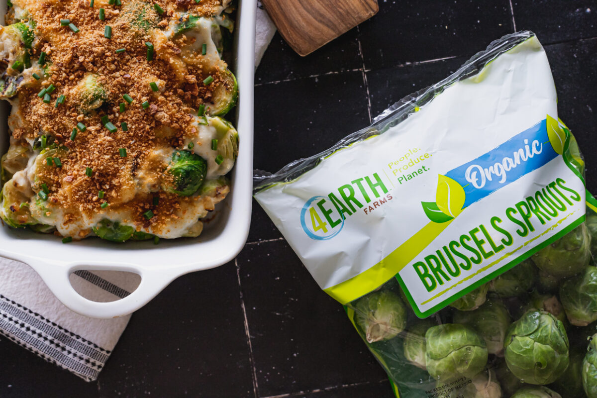 A dish of Brussels casserole on a black tile counter next to a bag of Brussels sprouts