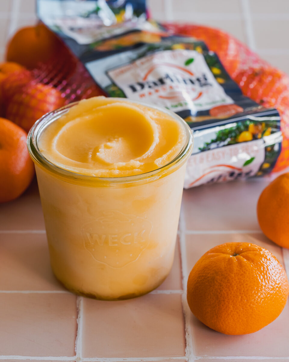 A glass container filled with clementine sorbet with a bag of clementines in the background