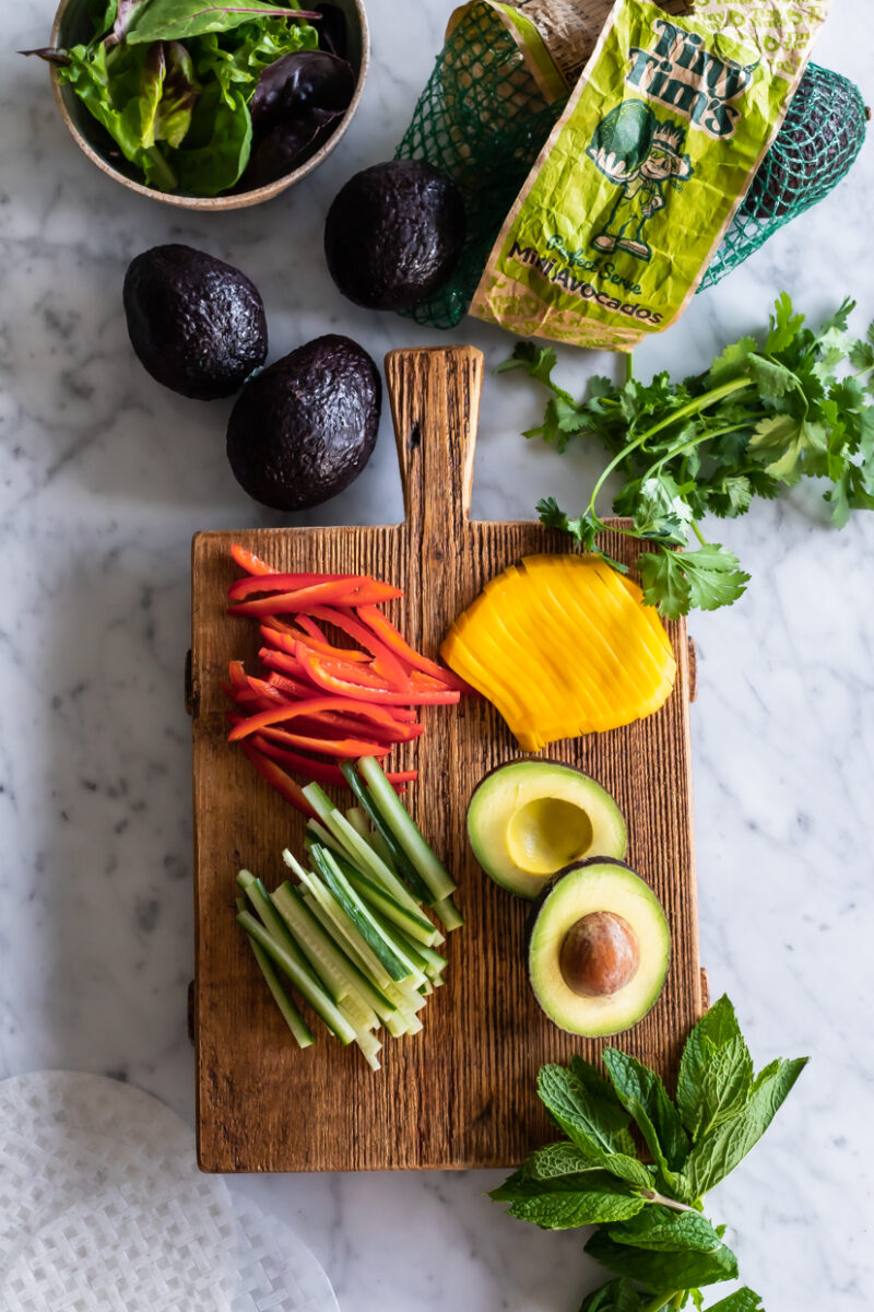 ingredients for avocado summer rolls on a wood cutting board on a marble table