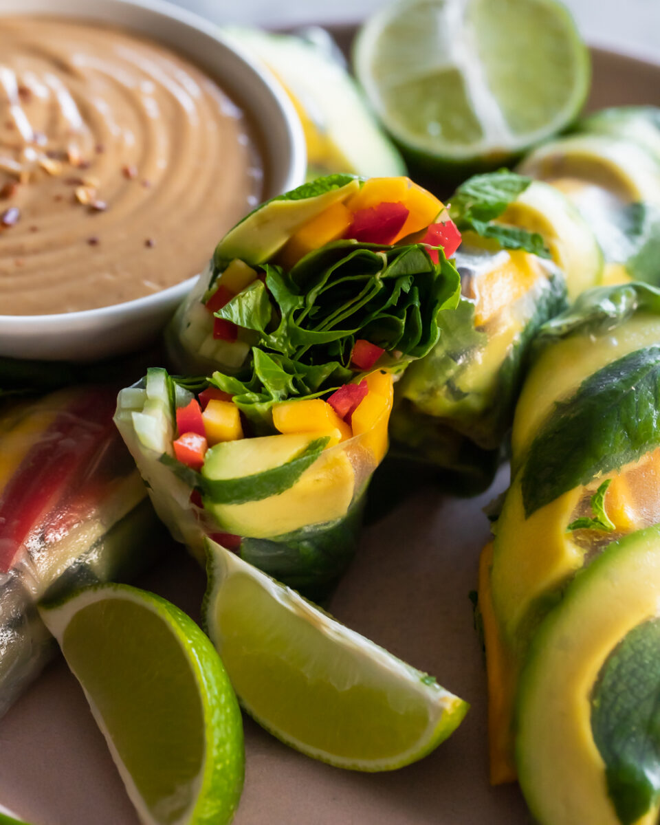 an avocado summer roll cut inhale lengthwise to show the colorful interior ingredients: mixed greens, avocado, mango, cucumber and bell pepper